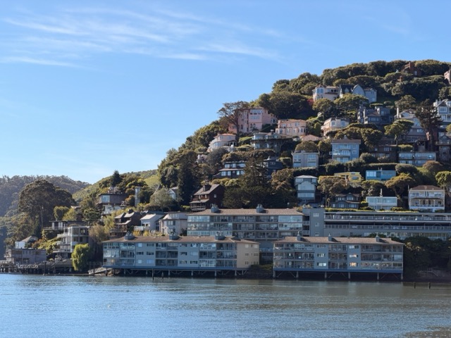 View of houses dotting a green hill as seen from Bridgeway in Sausalito